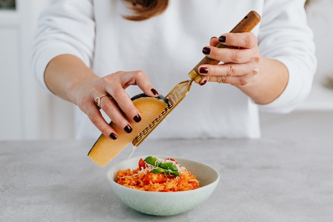 Someone grating cheese over a bowl of pasta