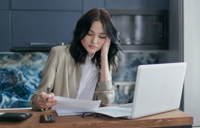 Asian woman at laptop looking at paperwork