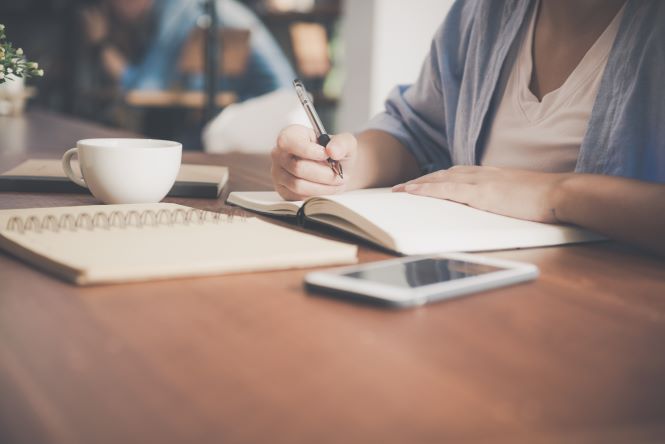 Person with cup of coffee doing calculations in a notebook