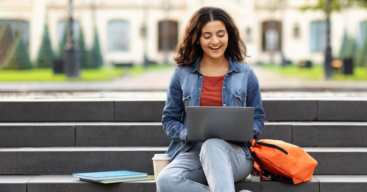 Happy college student checking student loan options on her laptop outside.