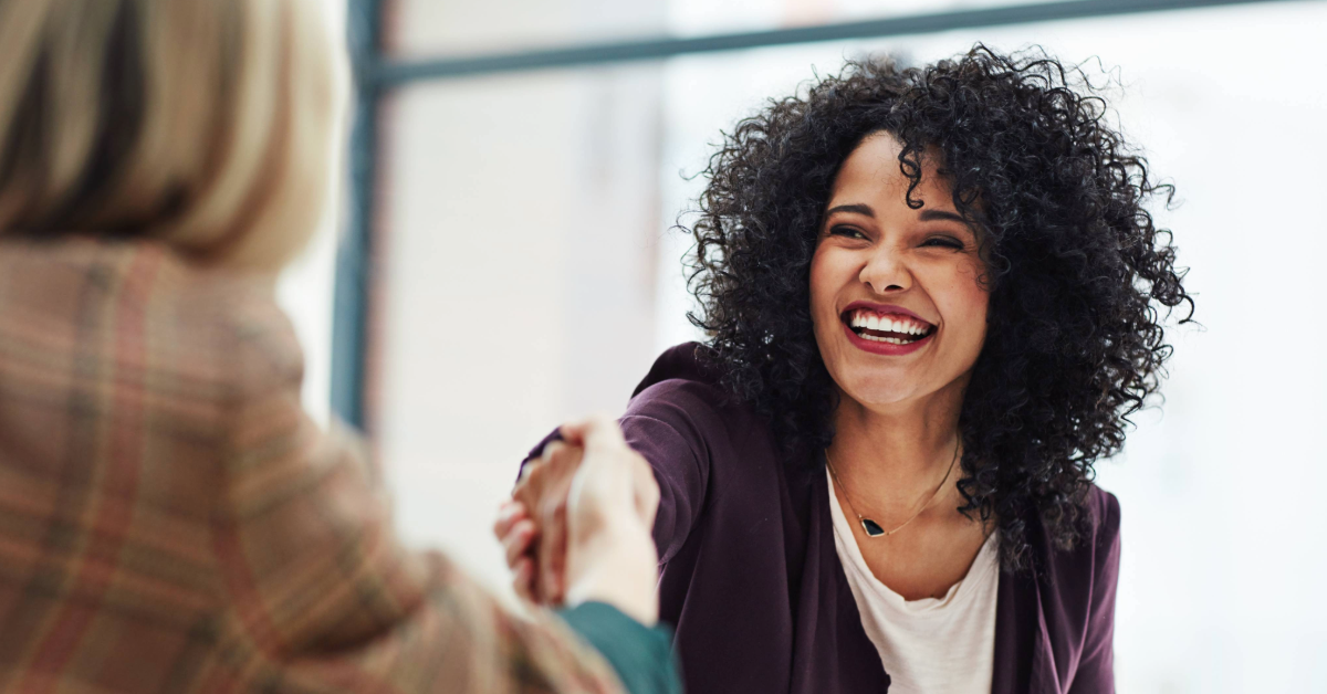 Black woman smiling and shaking hand with another woman